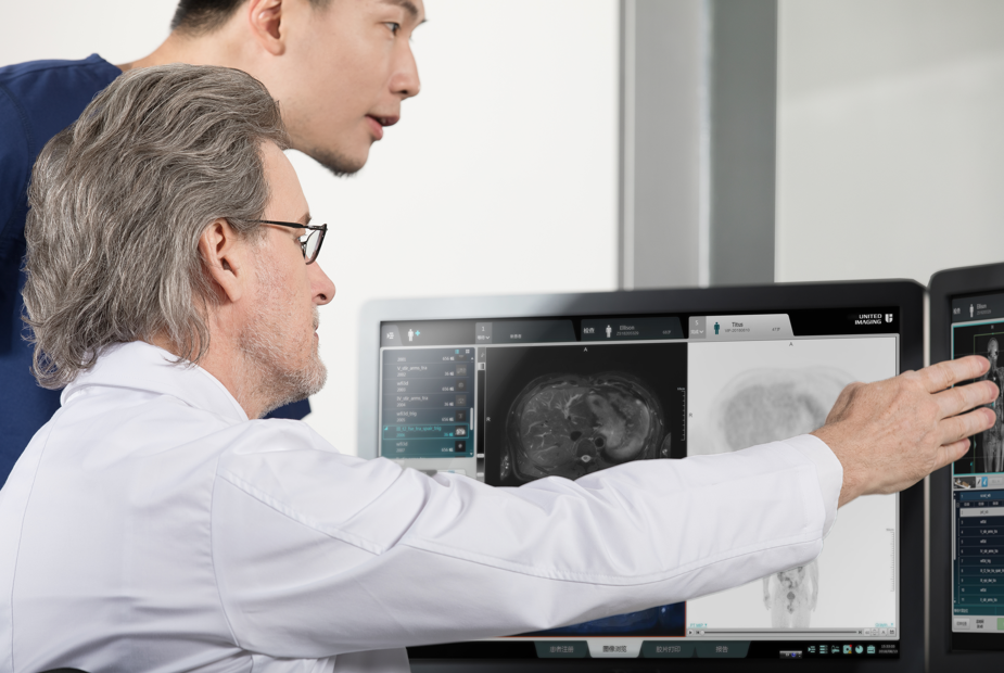 A resident MD in blue looks on as a Radiologist teaches about diagnostic imaging on a uMR 570 console. 